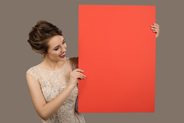 Charming happy woman holding big red paper empty blank. Gray background.