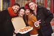© Evgeniy Kalinovskiy - group of friends with a box of pizza smiling and eating pizza on the street