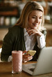 © Drazen - Smiling businesswoman typing text message on mobile phone while using laptop in a cafe.