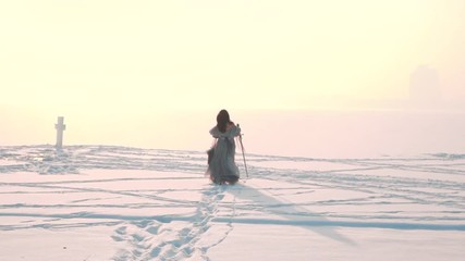 Wall Mural - gorgeous slow-motion on winter landscape, charming girl with dark flying hair runs through snow in long gray light vintage fluttering dress, holds dress hem in front of her and sword in hand, no face