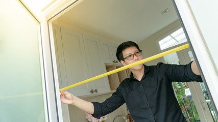 Young Asian worker man using tape measure on door frame in the kitchen. Home interior designer measuring elements on site. Housing design and construction concept