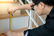 Young Asian worker using tape measure for measuring riser and thread on stair in the house. Housing staircase construction and renovation.