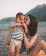 © ASTA Concept - Young mother with her little baby girl have fun sitting on a beach in summer day at sunset over mountains. Happy family concept. Happy childhood