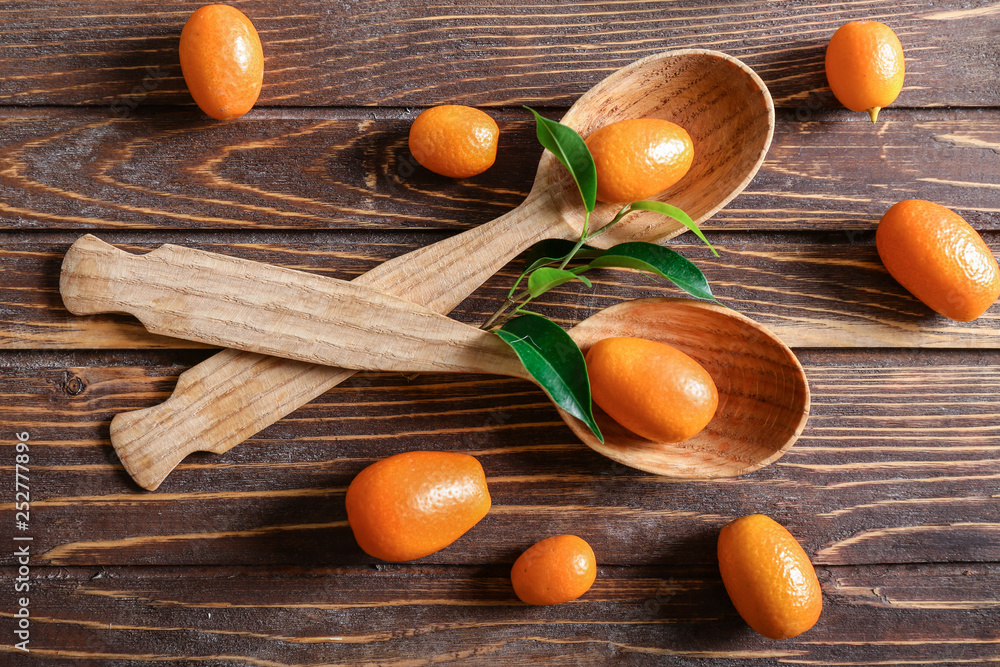 Spoons with delicious kumquat fruit on wooden table