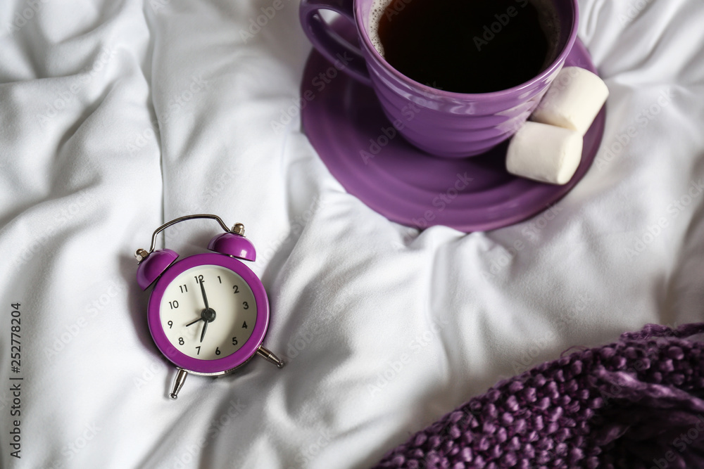 Alarm clock and cup of coffee on bed in morning