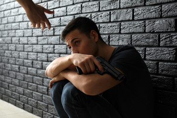 Wall Mural - Woman giving hand to depressed man with gun near dark wall. Suicide prevention concept