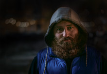 Bearded Man In Blue Sports Wear And Hood Looks At Camera Under Night City Lites