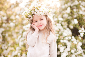 Wall Mural - Cute baby girl 4-5 year old wearing floral wreath standing over flower background. Looking at camera. Spring season.