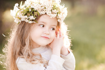 Wall Mural - Funny baby girl 3-4 year old wearing flower wreath outdoors over green background. Childhood. Spring season.