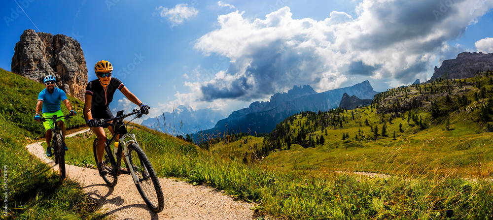Cycling woman and man riding on bikes in Dolomites mountains landscape. Couple cycling MTB enduro trail track. Outdoor sport activity. - obrazy, fototapety, plakaty 