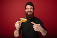 Young Bearded Man Over Red Wall Holding Credit Card Very Happy Pointing With Hand And Finger
