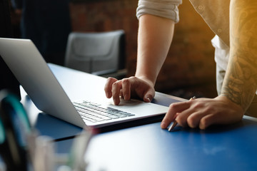 Wall Mural - Male hands working on a computer, on a blue table, against the backdrop of a modern office with sunlight