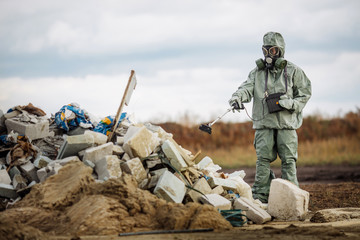 radiation supervisor in protective clothing and gas mask with geiger counter checks the level of radioactive radiation in the danger zone