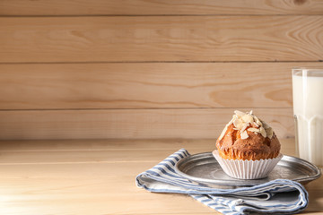 Plate with tasty almond muffins and milk on wooden table