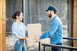 © rh2010 - Delivery man bringing packaged goods to a young woman client standing together outdoors in front of the modern house.