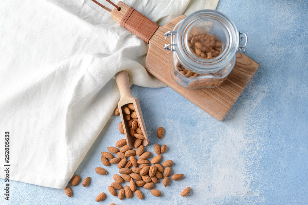 Scoop and jar with tasty almonds on color table
