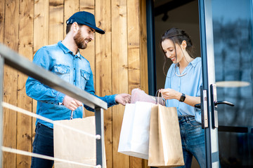 Delivery man bringing some goods packaged in paper bags for a young woman client to home. Buying clothes online and delivery concept