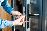Man changing core of a door lock of the entrance glass door, close-up view with no face