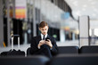 © Seventyfour - Portrait of young businessman using smartphone sitting on leather chair in airport, copy space