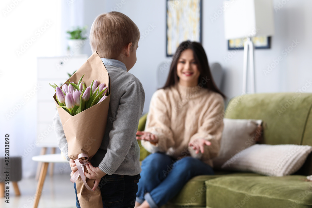 Little boy hiding flowers for his mother behind back. 8 March celebration