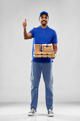 Wall Mural - service and people concept - happy indian delivery man with food and drinks in blue uniform showing thumbs up over grey background