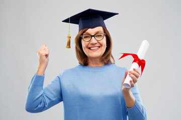 Wall Mural - graduation, education and old people concept - happy senior graduate student woman in mortar board with diploma laughing over grey background