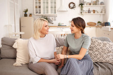 Beautiful Happy Mature Mother And Her Adorable Cute Daughter Spending Time Together After Long Separation, Sitting In Cozy Living Room Interior And Talking, Looking At Each Other And Smiling