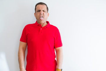 Middle age man wearing red t-shirt over white wall sticking tongue out happy with funny expression. Emotion concept.