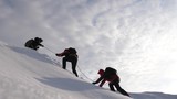 Fototapeta Natura - Travelers climb rope to their victory through snow uphill in strong wind. tourists in winter work together as team overcoming difficulties. three Alpenists in winter climb rope on mountain.