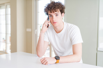 Young man talking on the phone at home with a confident expression on smart face thinking serious