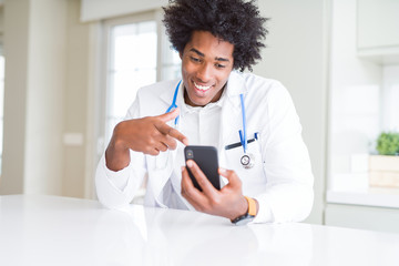 Wall Mural - african american doctor man using smartphone at the clinic very happy pointing with hand and finger