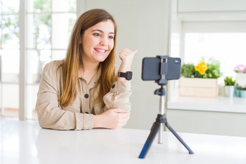 Poster - Beautiful young woman doing online video call using smartphone webcam smiling with happy face looking and pointing to the side with thumb up.