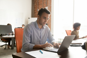 Focused mature businessman working with laptop documents in modern office