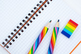 Fototapeta Tęcza - Open copybook with two rainbow-coloured pencils and a rubber on white wooden table