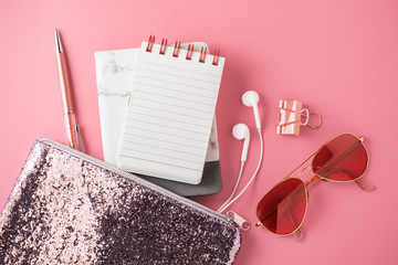 Wall Mural - Fashion glitter bag with note pad, sunglasses, earphone and pen on pink background