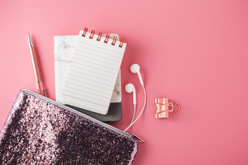 Wall Mural - Fashion glitter bag with note pad, earphone and pen on pink background, flat lay