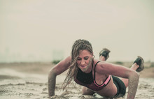 Closeup Of Strong Athletic Woman Crawling In Wet Muddy Puddle With Mud On Her Face In An Extreme Competitive Sport
