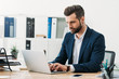 © LIGHTFIELD STUDIOS - businessman in blue suit sitting at table with laptop and typing in office
