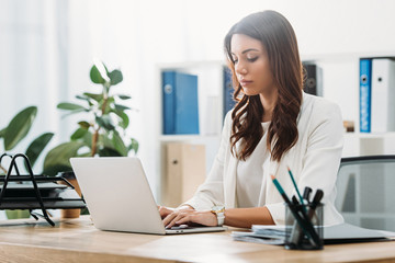 attractive businesswoman sitting at table with laptop and typing in office