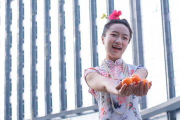 Young woman wearing traditional Chinese dress with two hands holding lucky oranges, happy Chinese new year