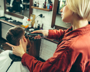 Wall Mural - Client during beard shaving in barbershop. Female barber at salon. Gender equality. Woman in the male profession.