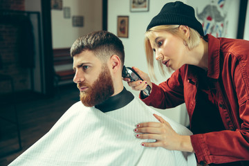 Wall Mural - Client during beard shaving in barbershop. Female barber at salon. Gender equality. Woman in the male profession.