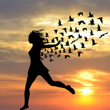 Silhouette Of Young Woman Jumping With Birds Flying From Her