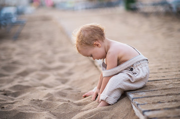 Wall Mural - A small toddler girl sitting on beach on summer holiday, playing.