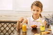Happy little girl of school age enjoying healthy breakfast eating sandwich and fruits and drinking orange juice sitting at bright sunny kitchen