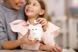 © Kalim - Young girl and her mother with piggybank sitting at table