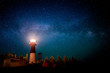A lighthouse at night with a star filled sky above. The light in the top of the lighthouse is illuminated. The Milky Way is visible.
