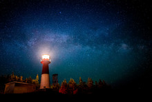 A Lighthouse At Night With A Star Filled Sky Above. The Light In The Top Of The Lighthouse Is Illuminated. The Milky Way Is Visible.