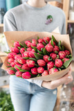 Fototapeta  - Young beautiful woman holding a spring bouquet of red tulips in her hand. Bunch of fresh cut spring flowers in female hands