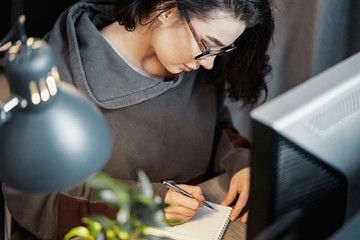 Attractive woman freelancer writer thinking about text and writing in note pad.